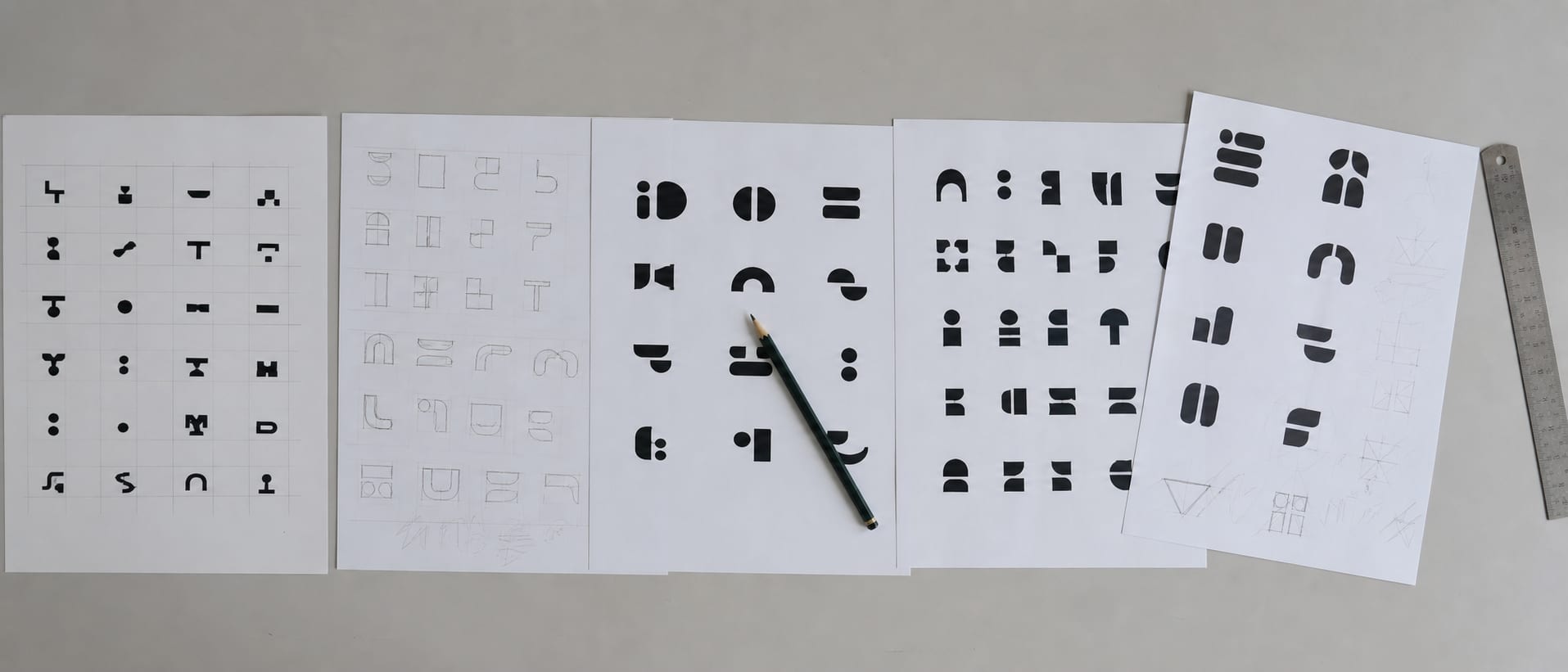 A wide strip of a studio table carrying printed wordmark trials in black on white, arranged in a row and slightly overlapping, with a pencil laid across them