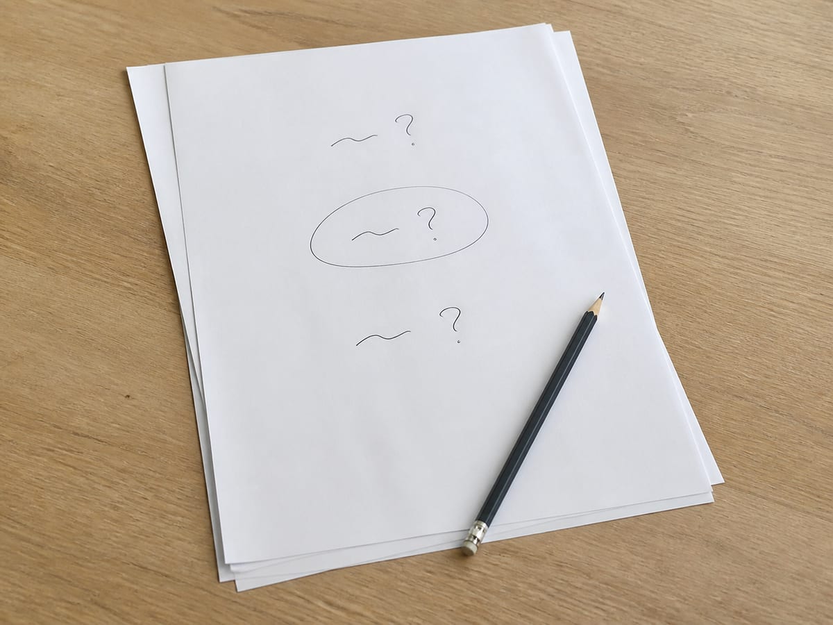 A sheet of paper carrying three short handwritten questions, one circled, resting on a plain desk