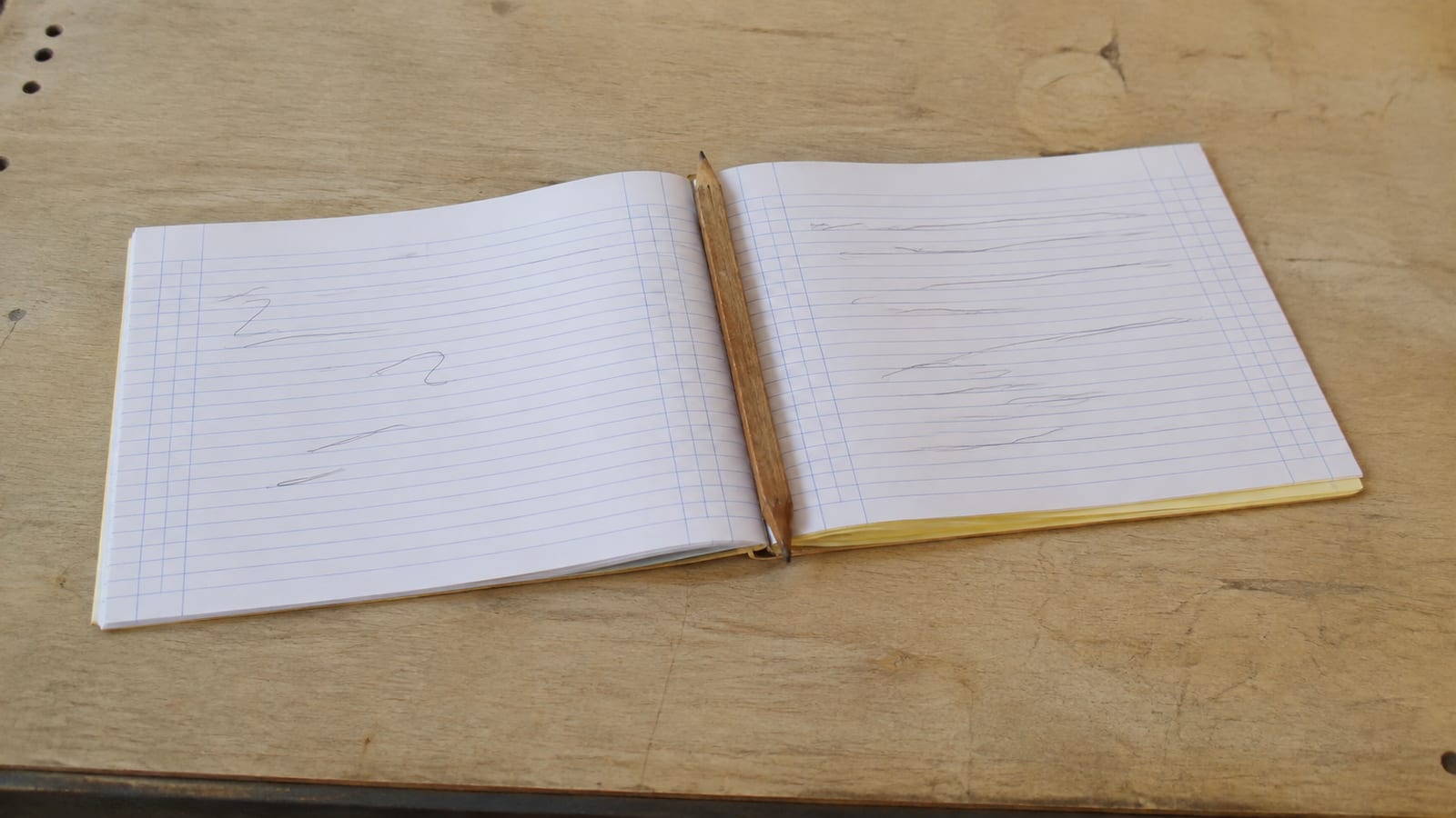 A carbon-copy duplicate job book open flat on a workbench surface, the top docket filled in by hand in ballpoint, its yellow second copy showing beneath, a worn pencil laid across the spine