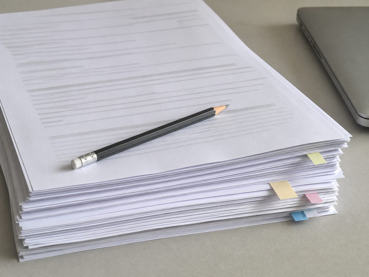 A thick stack of printed sheets on a desk, slightly fanned, with a few coloured tabs marking places part way down