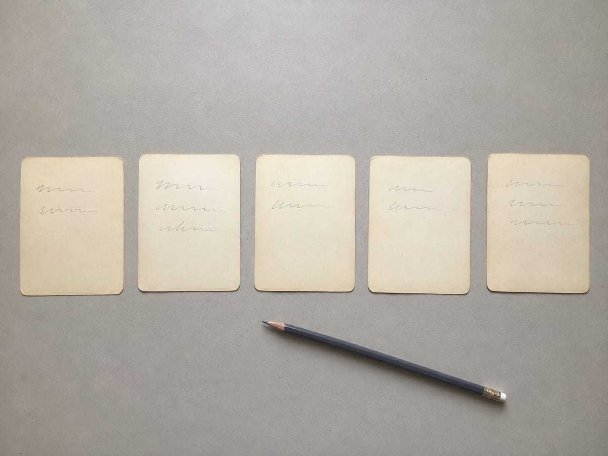 A small run of index cards laid out in a single row on the desk, evenly spaced, each carrying two or three short handwritten lines