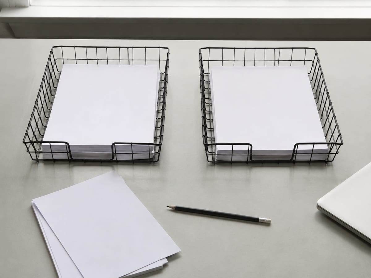 Two wire desk trays set side by side on the desk rather than stacked, each holding a modest and roughly equal bundle of dockets