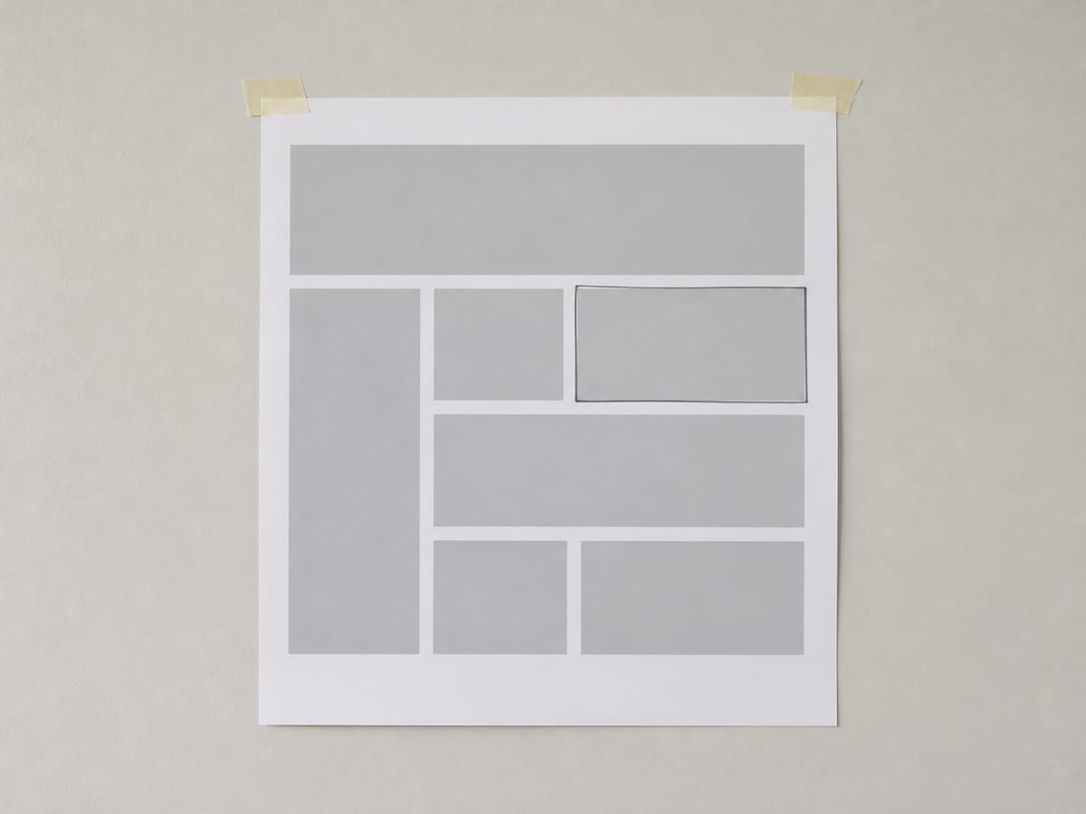 A single printed proof sheet held upright against a plain wall by two small strips of masking tape, seen straight on, one block on it ringed in pencil