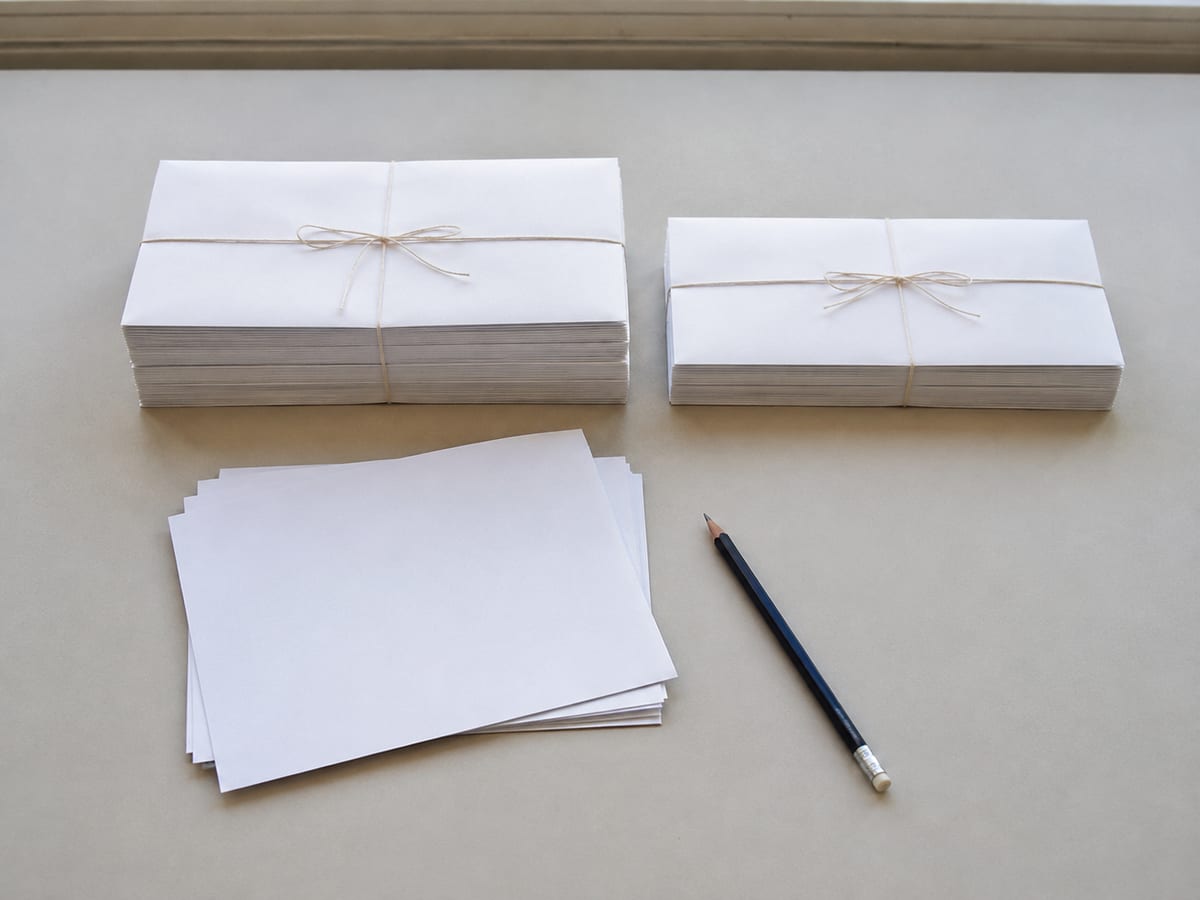 Two plain envelope bundles set side by side on the desk, each tied with string, one noticeably thicker than the other