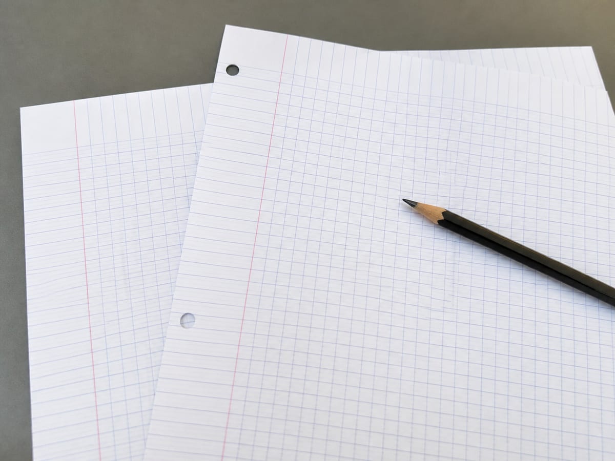 Two sheets of ruled analysis paper overlapping on the desk at a slight angle, their grid lines visibly failing to line up where they cross