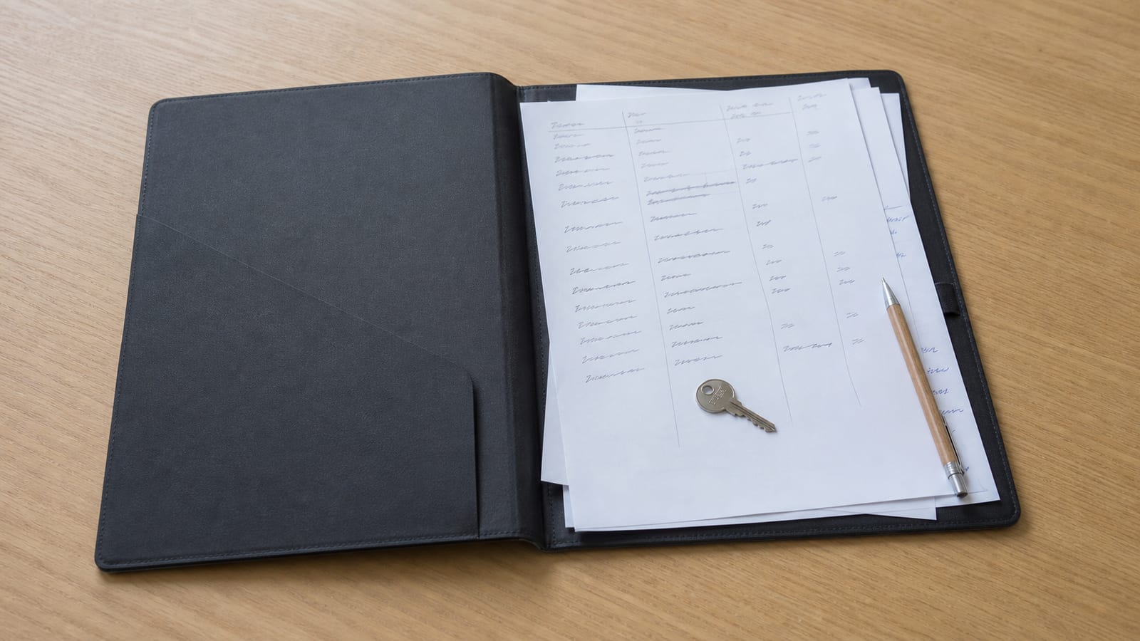 A plain document wallet open on a desk holding printed domain and hosting account records, a single small key resting on the top sheet, nothing else in frame