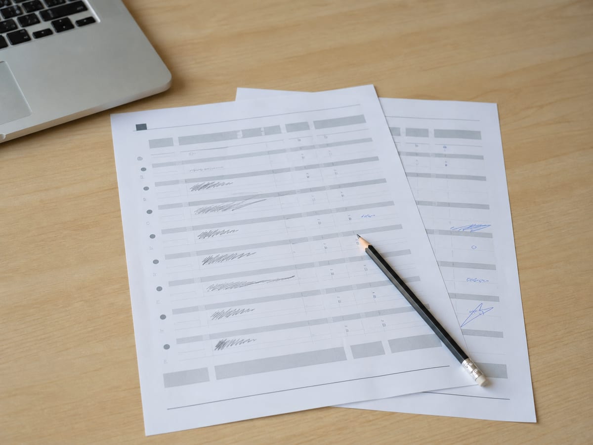 A printed list of page questions on a desk with several lines marked in pencil, a second sheet fanned beneath it