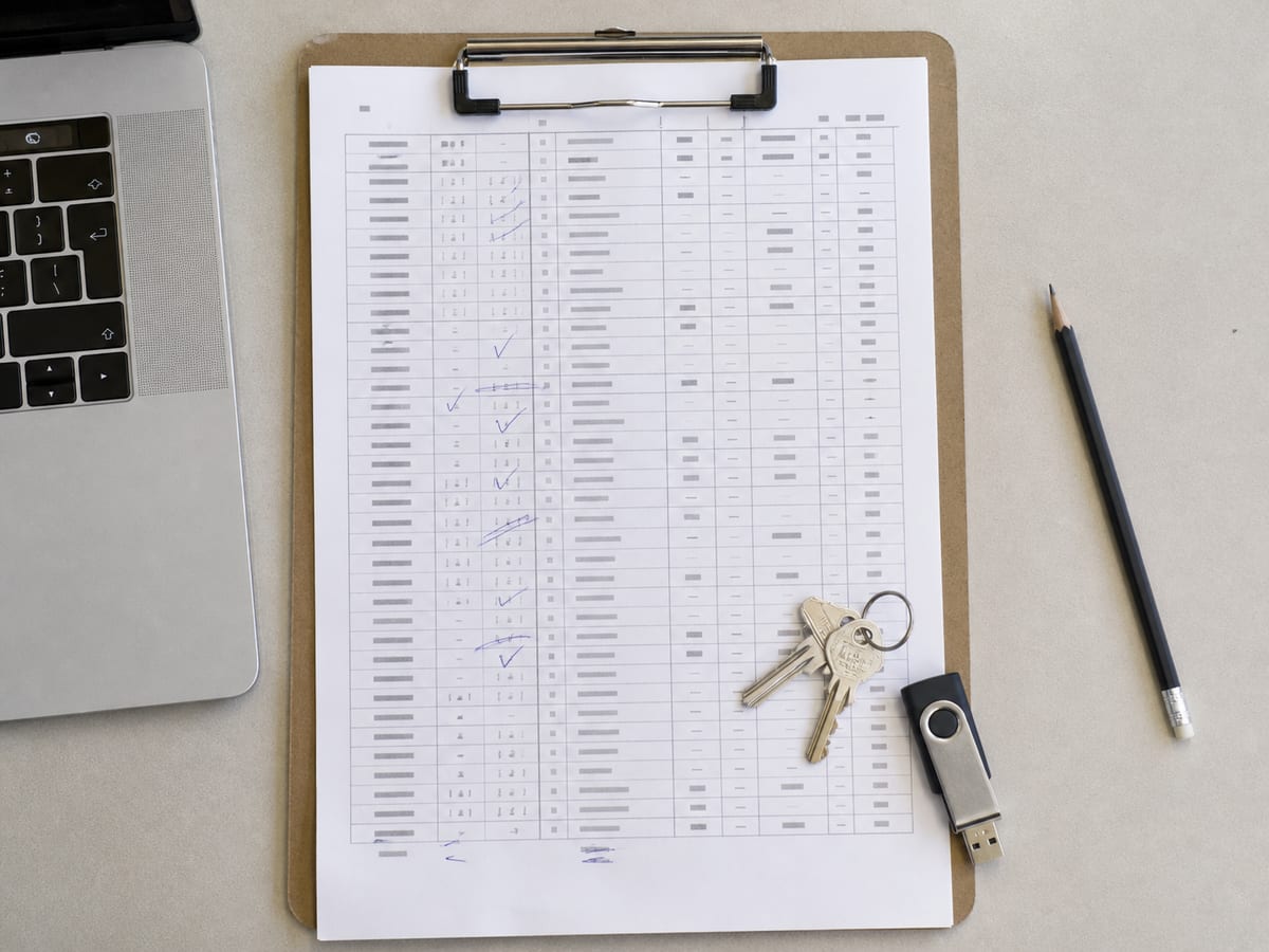 A printed redirect table on a clipboard, rows ticked in pen, a USB drive and a set of keys resting on the corner of the sheet